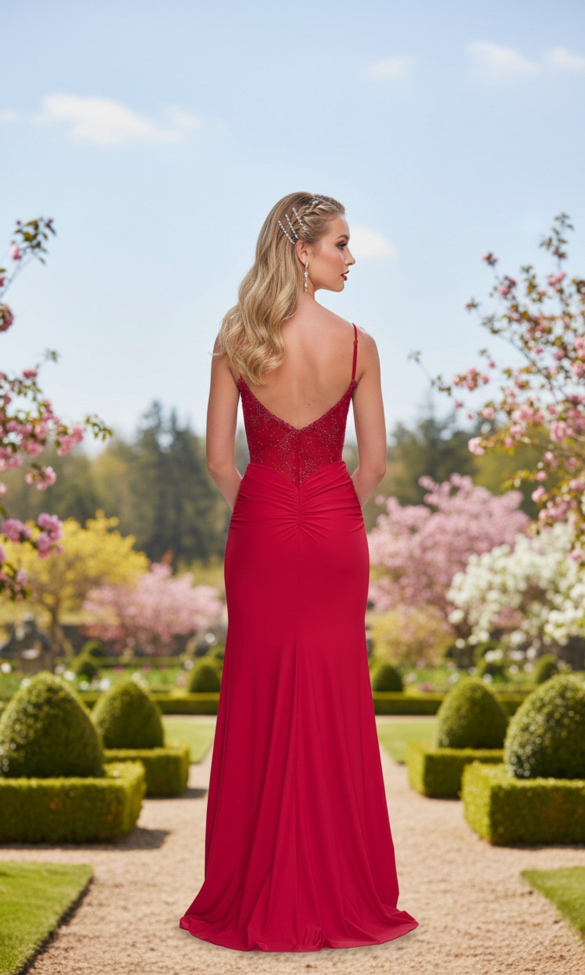 Wearing the Lace-Corset Long Prom Dress: La Femme 33395, a woman stands on a garden path lined with manicured bushes and blooming trees, showcasing the gown’s elegant low back.
